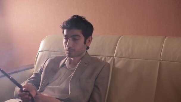 Бизнесмен курит кальян и отдыхает на диване в уютной комнате . — стоковое видео