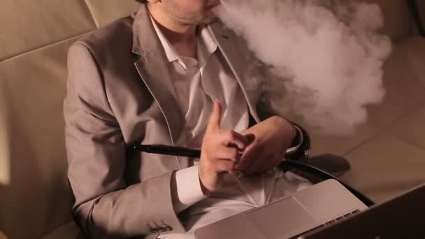 Businessman smoking hookah and working at a laptop. — Stock Video