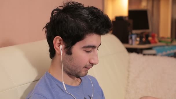 Jeune homme avec écouteurs écoutant de la musique dans la chambre . — Video