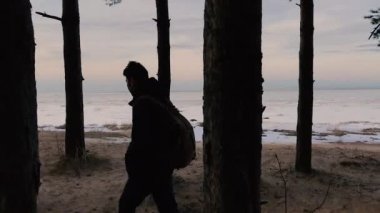 Ağaçlar koyu arka planda ve kıyı boyunca insan bir sırt çantası ile yürüyor.