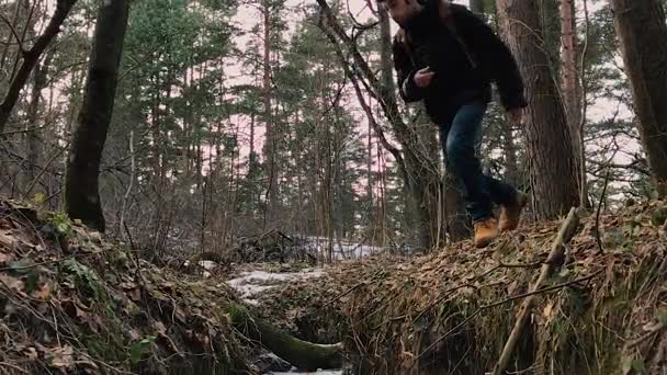 Homem com uma mochila salta sobre uma vala . — Vídeo de Stock