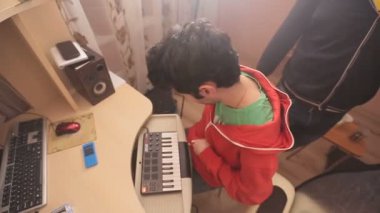 Bilgisayar ve MIDI klavye oturan genç adam. Müzik ve kollarını sallayarak dinliyor.