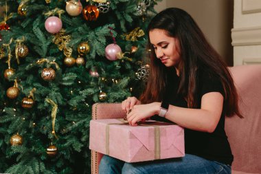 Güzel genç esmer kadın kanepe üzerinde Noel ağacı yakınındaki hediye paketini açmalısınız. Stüdyo yatay dikey.