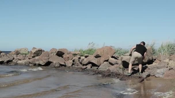 Mann wirft Stein ins Meer — Stockvideo