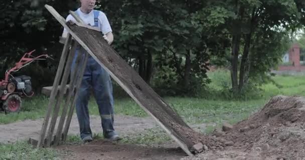 Travailleur de la construction tamisant le gravier à travers un tamis avec une pelle . — Video