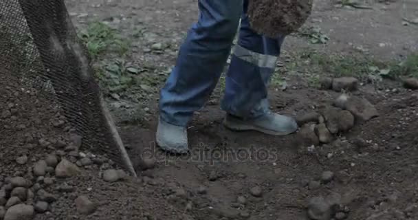 Будівельник просіює гравій через сито лопатою . — стокове відео