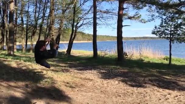 Un hombre balanceándose en un columpio improvisado sobre un árbol. árbol cuerda swing palo — Vídeo de stock