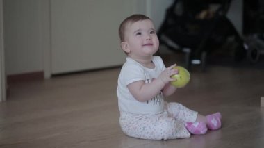 Evde katta oturan elinde yeşil elma ile küçük gülen bebek