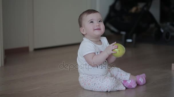 Piccolo bambino sorridente con mela verde in mano seduto sul pavimento a casa — Video Stock