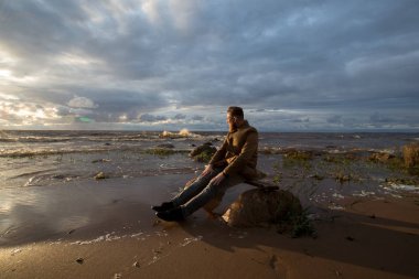 gün batımında sahilde oturmuş sakallı adam