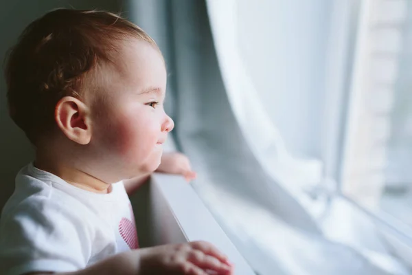 Little baby holds onto the bed and looks somewhere. — Stock Photo, Image