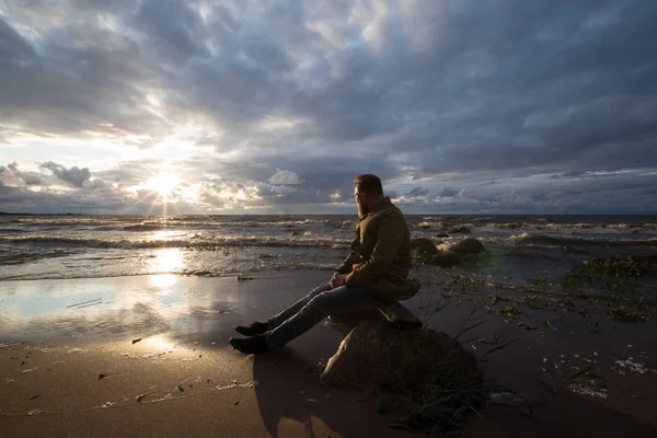 Bärtiger Typ sitzt bei Sonnenuntergang am Strand — Stockfoto