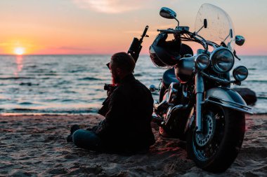 gün batımında sahilde Bisiklet yakınındaki otomatik silahlarla motorcu