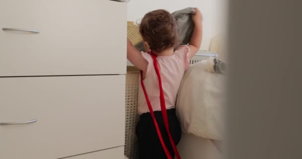Маленький ребенок вытаскивает одежду из корзины — стоковое видео
