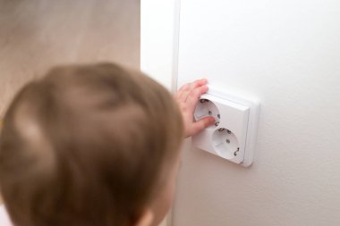 Küçük çocuk bir elektrik prizine evde arıyor. Çocukların güvenliği için
