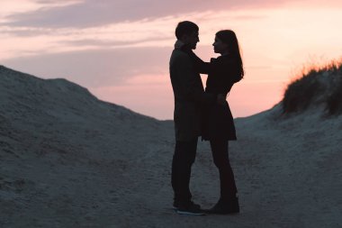 genç bir çift deniz kenarında sonbaharda gün batımında sarılma.