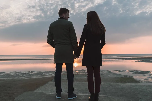 Joven pareja amorosa cogida de la mano en la orilla del mar en otoño . — Foto de Stock