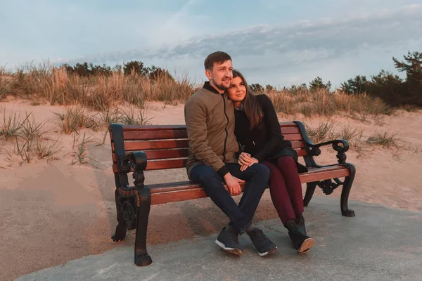 Jovem casal amoroso sentado em bancos perto da costa do mar no outono . — Fotografia de Stock