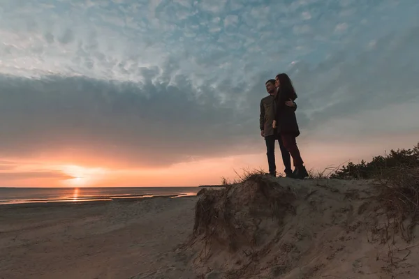 Joven pareja amorosa viendo la puesta de sol en el mar en otoño . — Foto de Stock