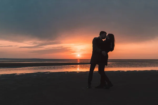 Jonge verliefde paar kussen zacht bij zonsondergang aan de kust in de herfst. — Stockfoto