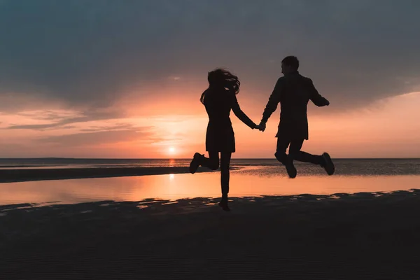 爱在秋天的日落时分跳跃在沙滩对年轻夫妇 — 图库照片