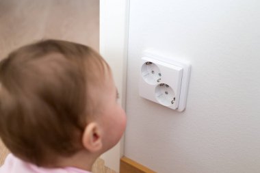 Küçük çocuk bir elektrik prizine evde arıyor. Çocukların güvenliği için
