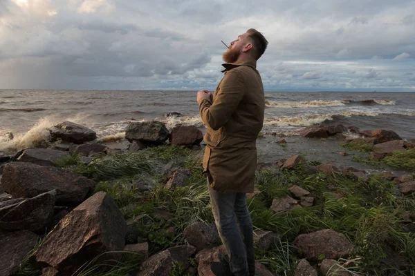 Fırtınalı havalarda sahil üzerinde bir sigara ile sakallı adam.