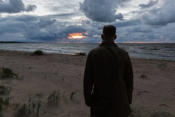 Brutaler Mann blickt auf den Sonnenuntergang am Meer. — Stockfoto