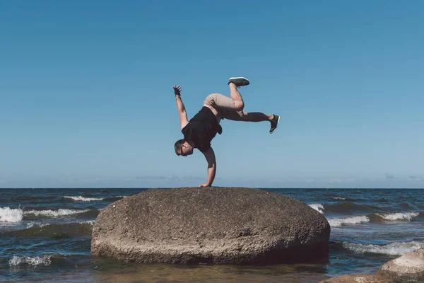 Hombre fuerte posando sobre una piedra sobre un fondo de una bahía y el cielo . — Foto de Stock