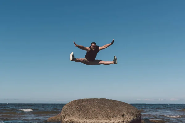 Starker Mann posiert auf einem Stein vor dem Hintergrund einer Bucht und des Himmels. — Stockfoto