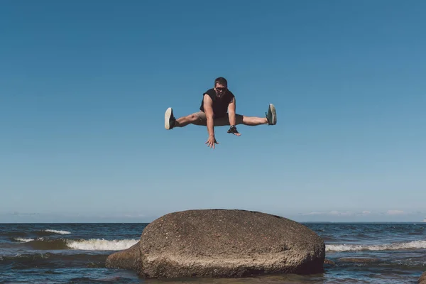 Starker Mann posiert auf einem Stein vor dem Hintergrund einer Bucht und des Himmels. — Stockfoto