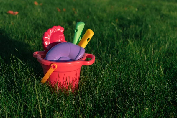 Crianças brinquedos coloridos em um balde em um gramado verde . — Fotografia de Stock