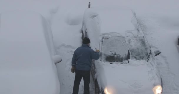 Мужчина чистит свой автомобиль от снега на парковке — стоковое видео