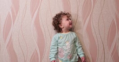 küçük kıvırcık saçlı çocuk evde duvara gülüyor