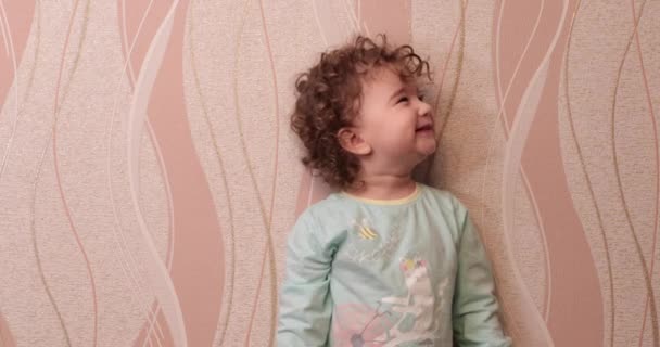 Küçük kıvırcık saçlı çocuk evde duvara gülüyor — Stok video