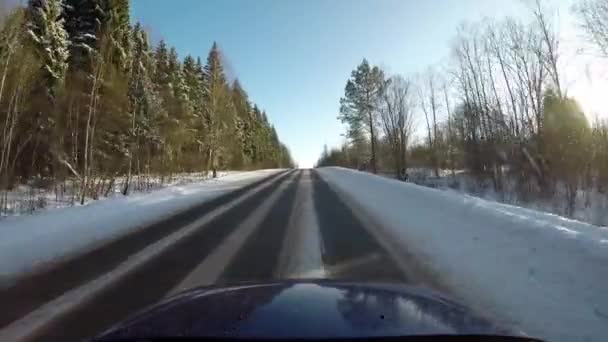 Conducir en coche en la carretera a través del bosque en invierno. Disparo en un día soleado gran angular — Vídeos de Stock