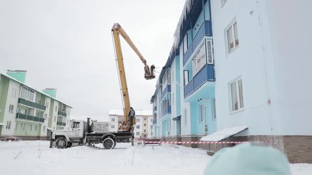 BEGUNITSY, LENINGRAD REGION, VOLOSOVO DISTRICT, RUSSIA - DECEMBER 7, 2017 Workers of housing and communal services bring down the icicles from the roof of a residential building. slow motion video — Stock Video