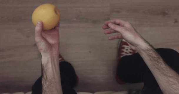 Guy zkoumá pečlivě pomeranč házet z ruky do ruky. Pohled shora videa 4k — Stock video
