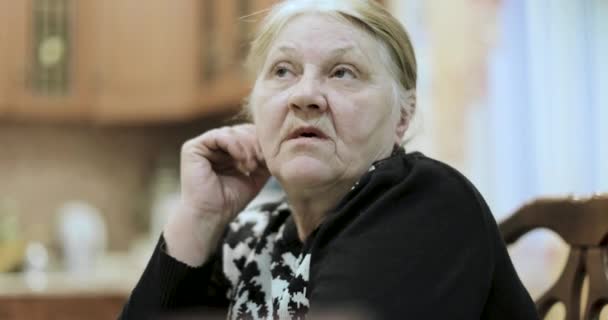 Старая бабушка рассказывает истории, сидя за столом — стоковое видео