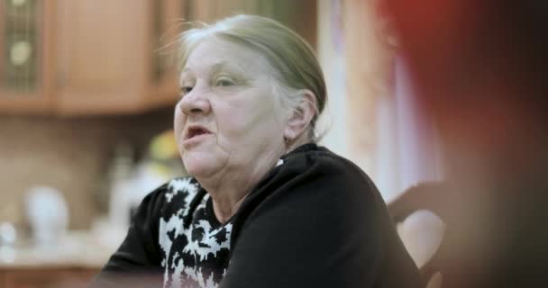 Стара бабуся розповідає історії, що сидять за столом — стокове відео