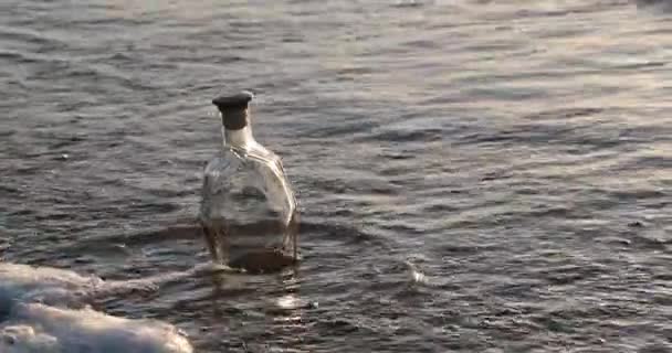 Lege glazen fles wast de golven van de zee in de avond — Stockvideo