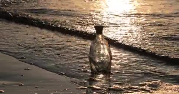 Άδειο γυάλινο μπουκάλι πλένει τα κύματα της θάλασσας το βράδυ — Αρχείο Βίντεο