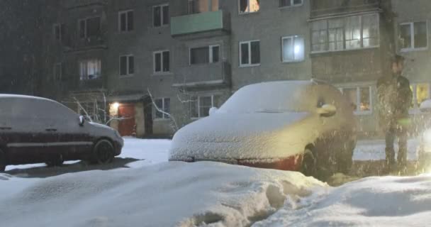 Hombre está de pie junto a un coche que ha sido llevado por la nieve — Vídeo de stock