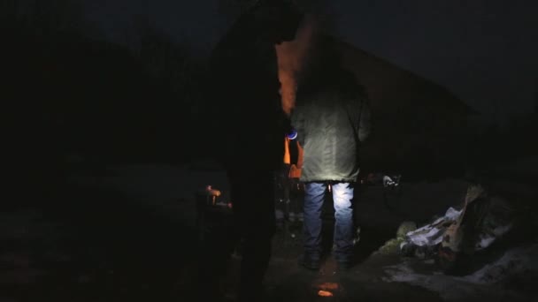 Один чоловік готує барбекю вночі інший сяє своїм ліхтарем — стокове відео