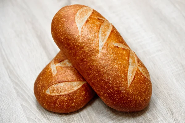 Twee versgebakken broden op een lichte houten achtergrond — Stockfoto