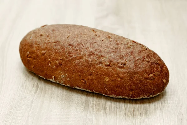 Jeden czarny chleb upieczony na jasnym tle drewnianych — Zdjęcie stockowe