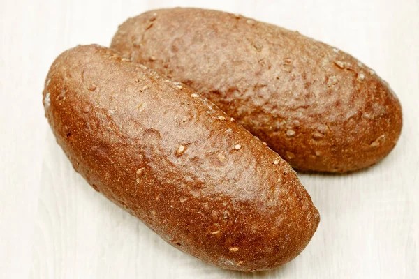 Two black baked bread on a light wooden background — Stock Photo, Image