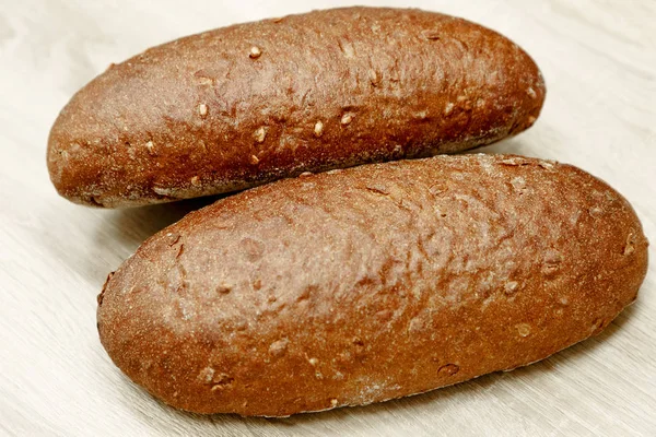 Two black baked bread on a light wooden background — Stock Photo, Image