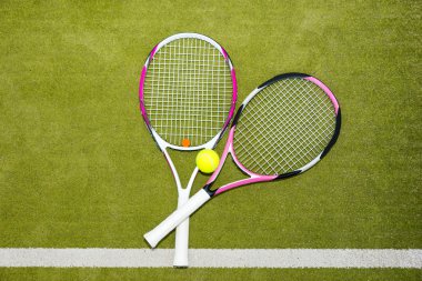 Yeşil çimenlerin üzerinde bir tenis topu ile iki yeni pembe tenis raketleri 