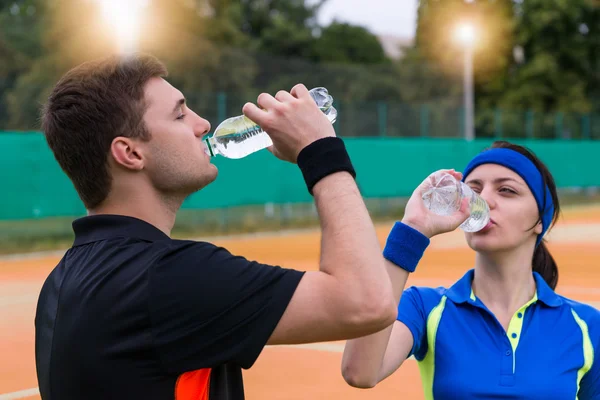 Pareja joven de tenistas bebiendo agua en cancha de barro outd — Foto de Stock